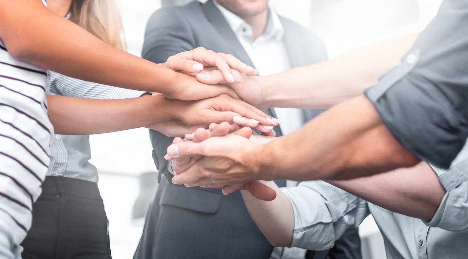 A group of business people joining hands to discuss employee benefits and group health insurance, guided by an experienced insurance broker in Singapore.